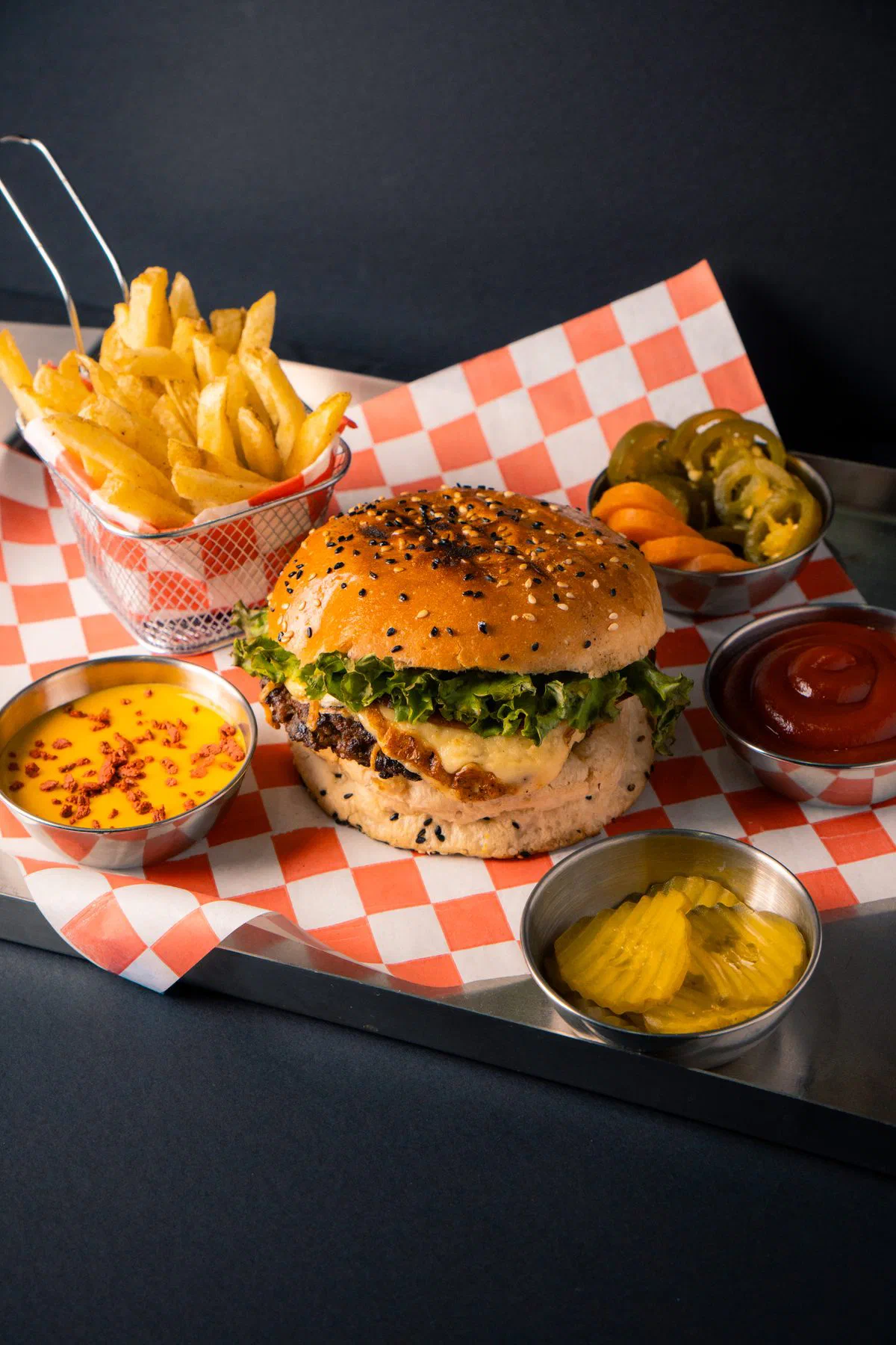 Hamburguesa con papas, pepinillos y salsas servida en charola